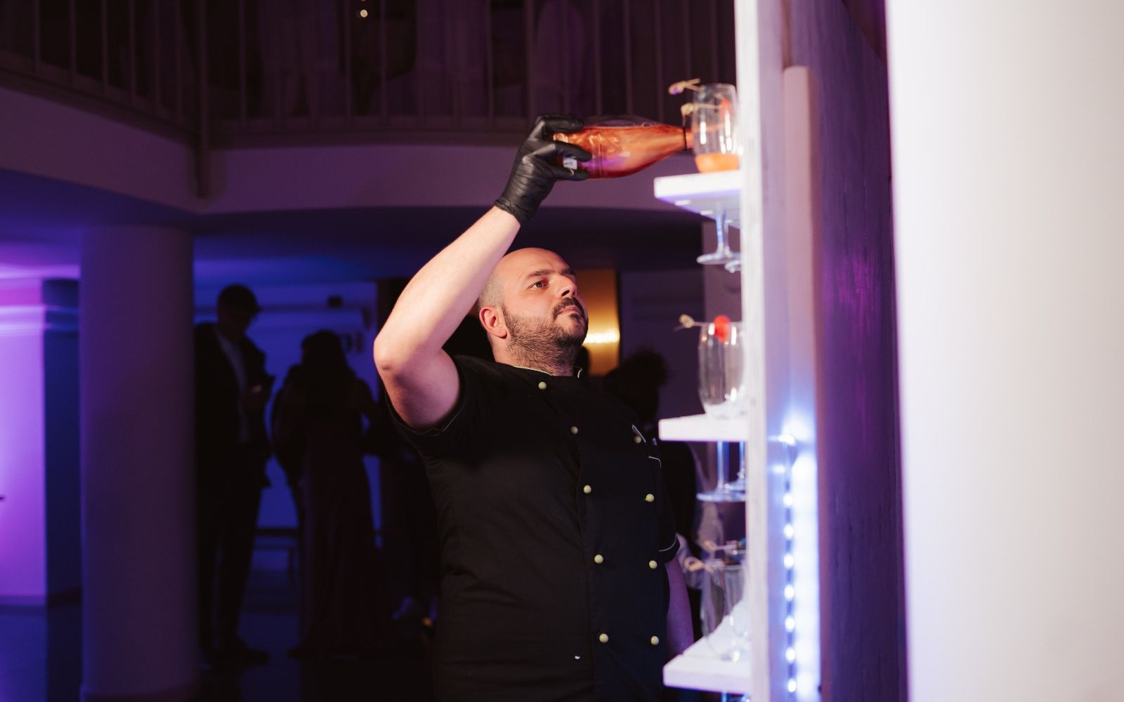 Il barman di Kokopelli versa un cocktail da una bottiglia sollevata, nel bar illuminato di viola