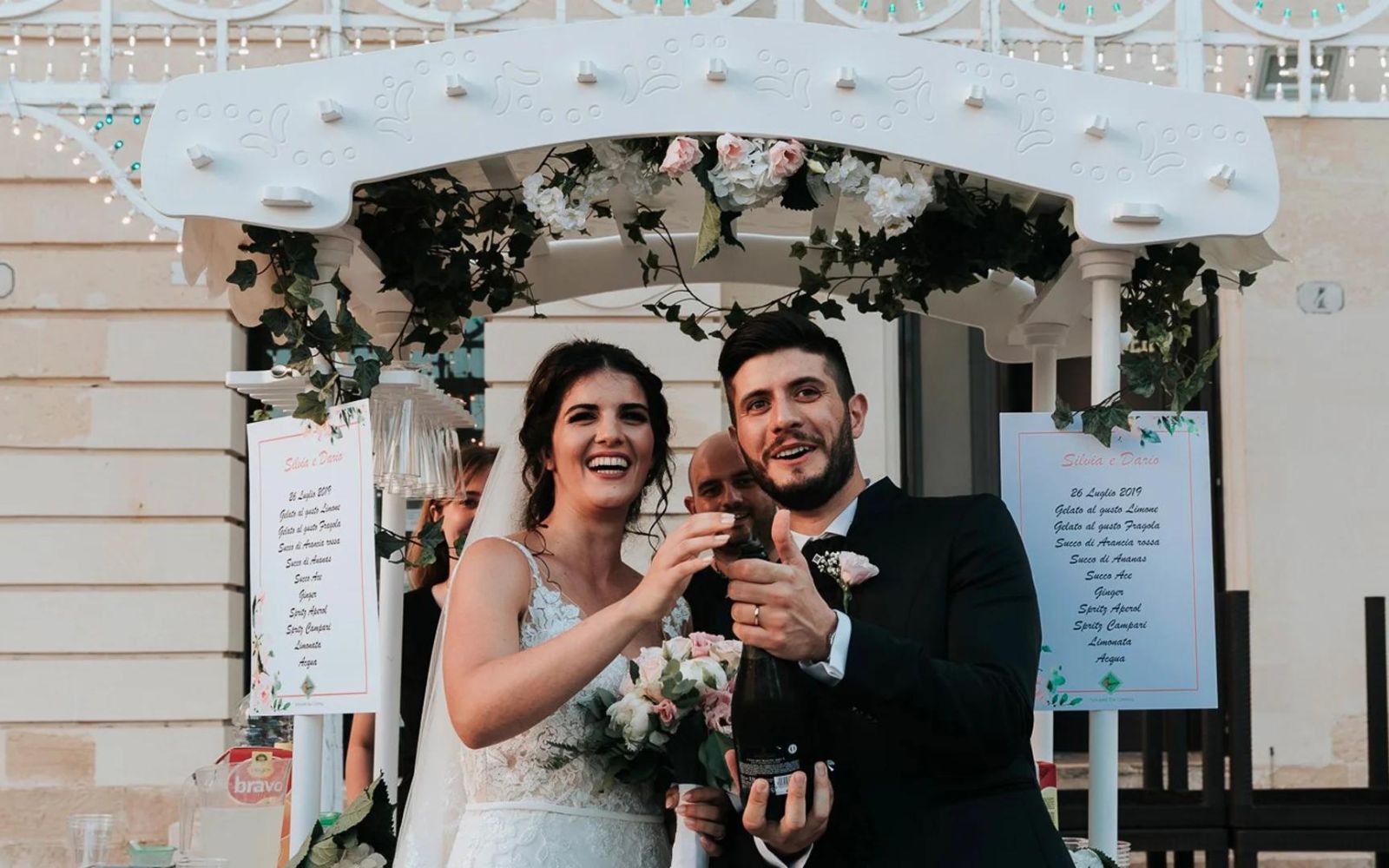 Gli sposi brindano davanti al carretto bianco con il gazebo di fiori
