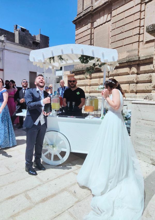 Sposi davanti al carretto bianco del rinfresco con le bevande fresche, in una piazza di paese