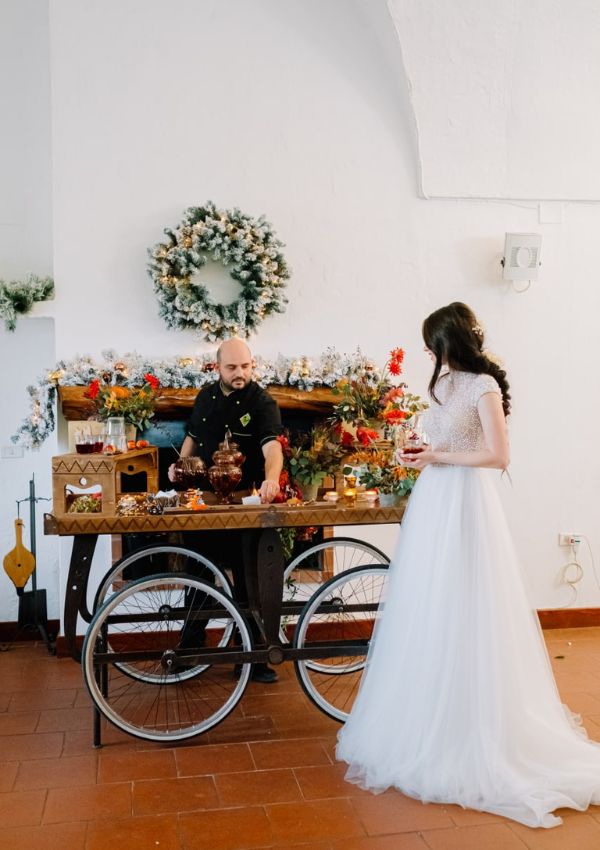 Il barman prepara i cocktail sul carretto in legno decorato con fiori, accanto alla sposa